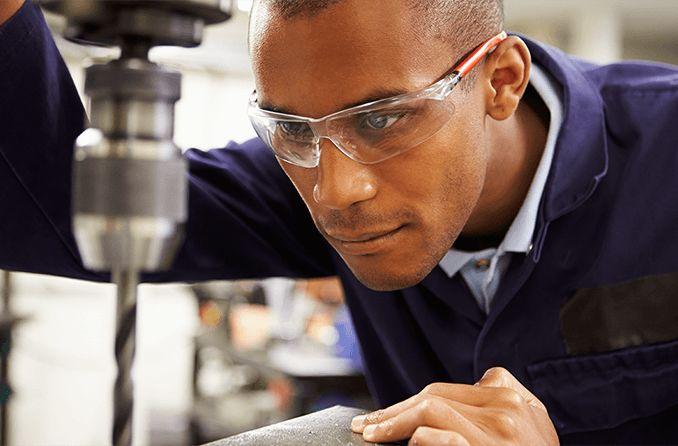 A man using a drill press while wearing safety glasses